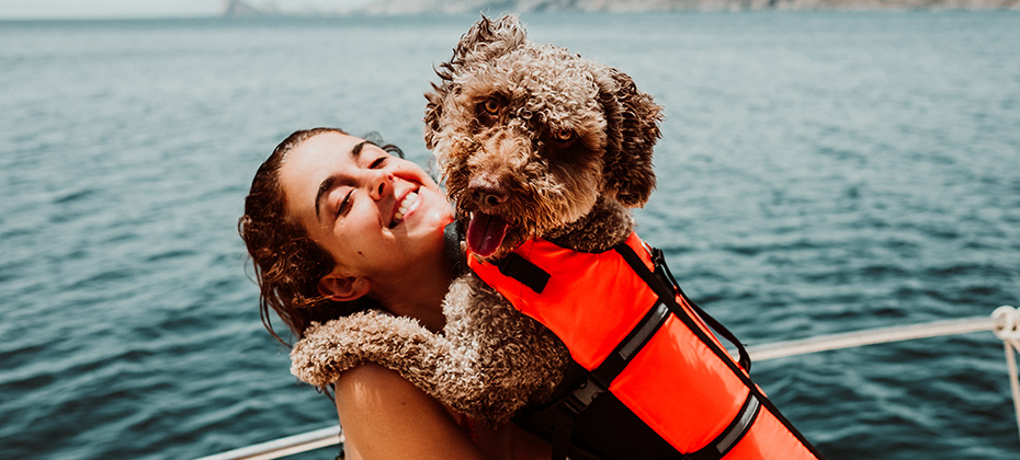 Young and attractive woman enjoying a relaxing vacation on her boat playing with her lovely brown spanish water dog on the yatch